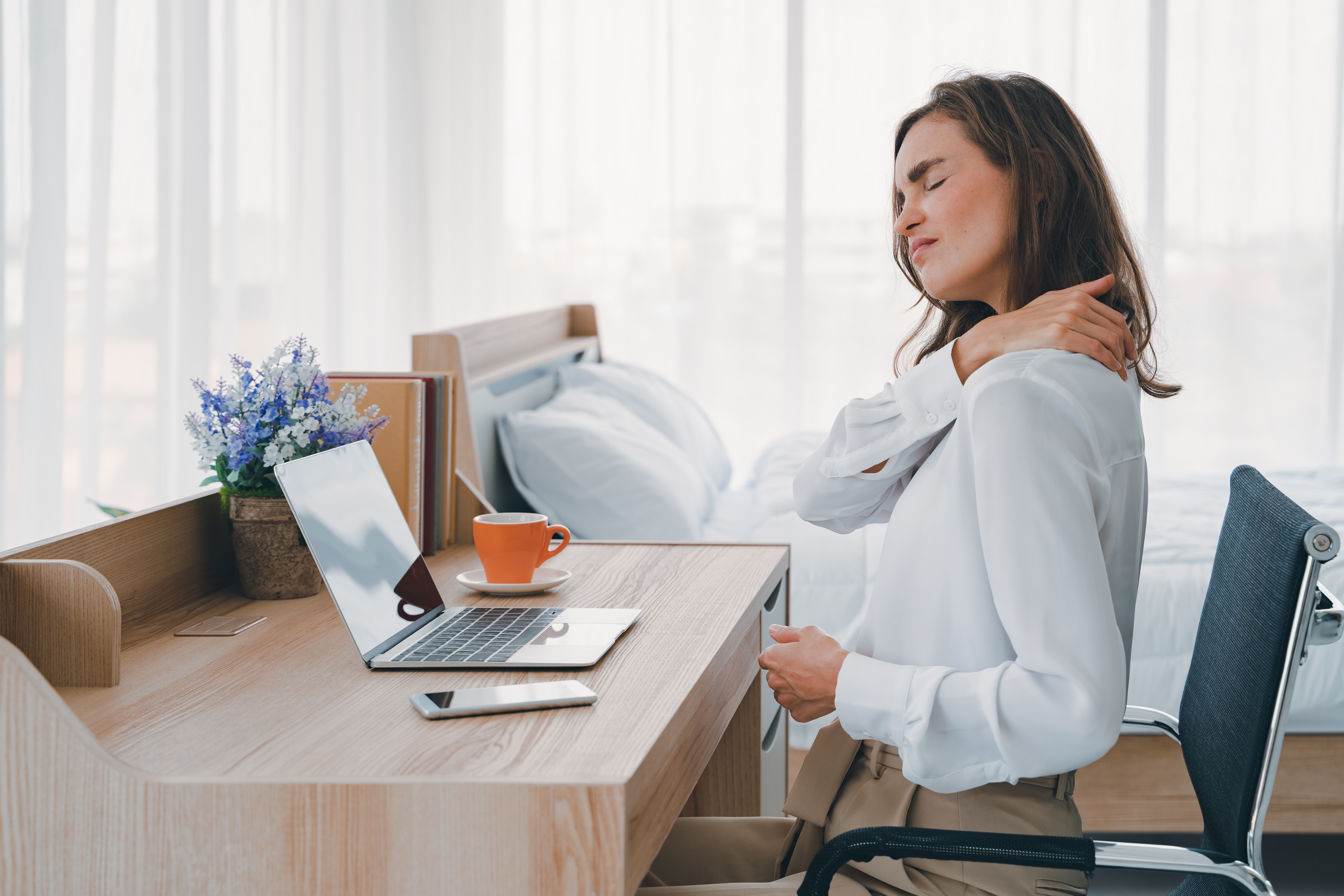Woman working at her desk, massaging her upper back due to pain