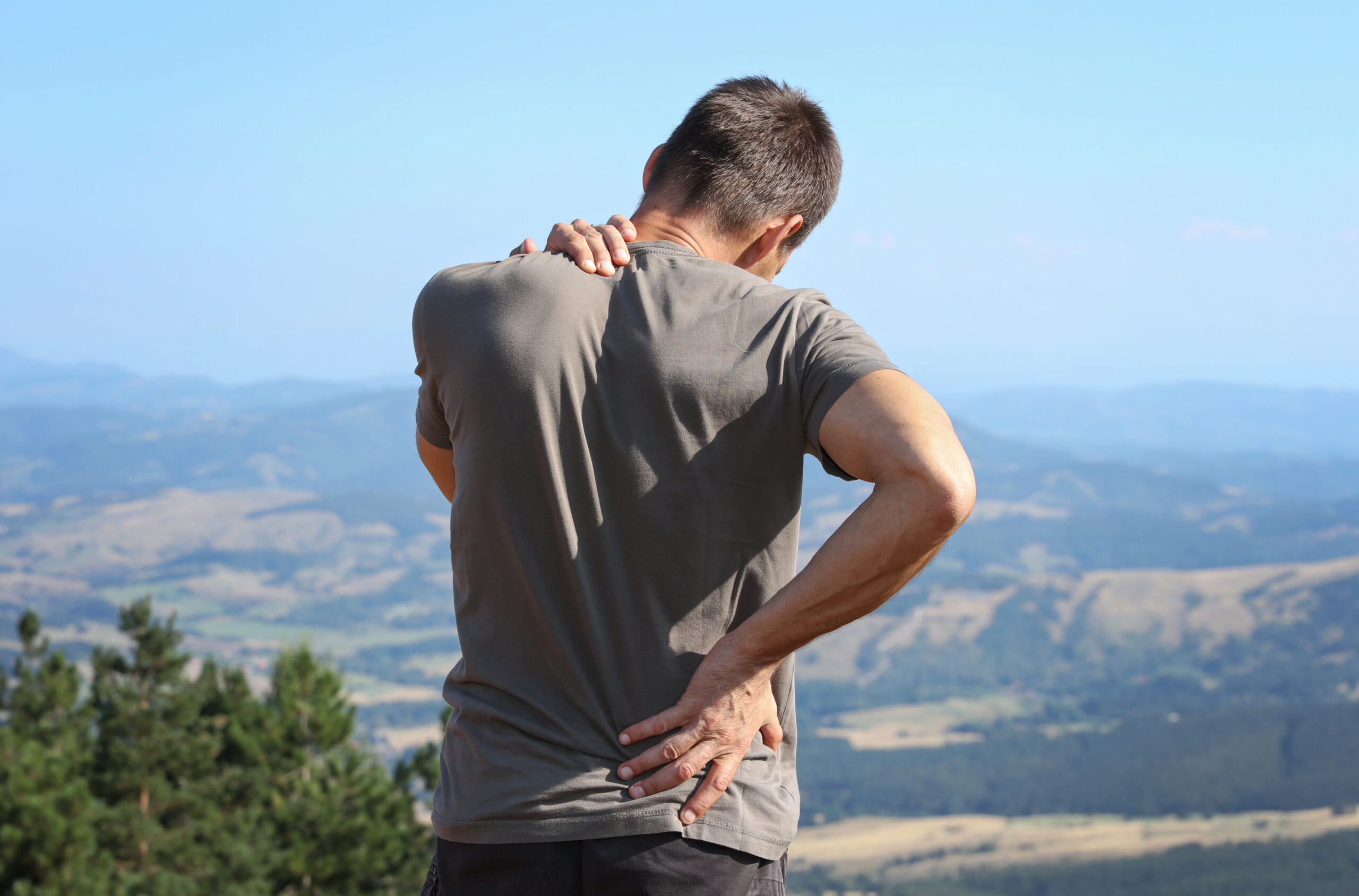 young male hiking in the mountains and is experiencing neck and lower back pain
